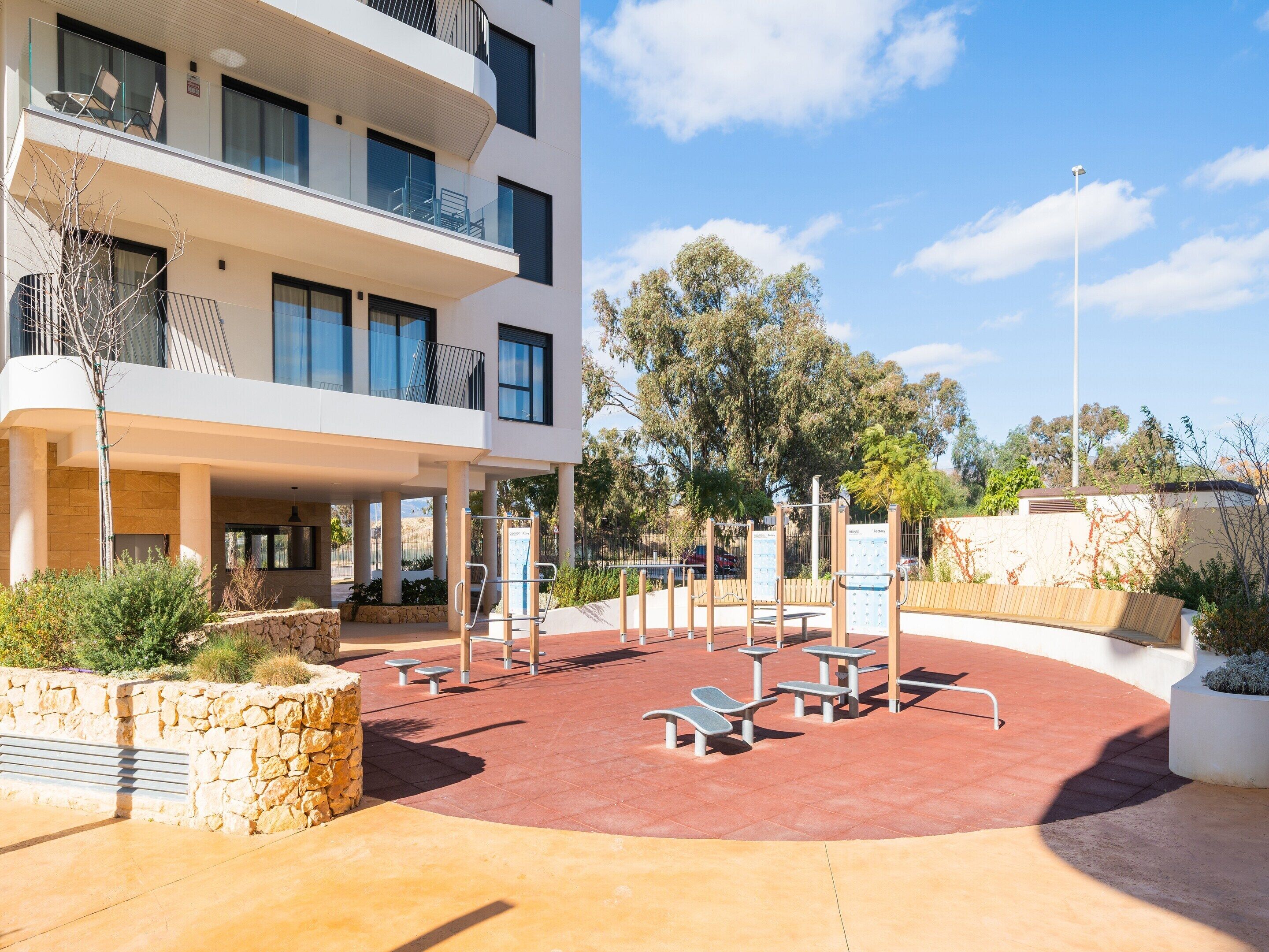 A modern building with a covered outdoor area featuring exercise equipment and seating.