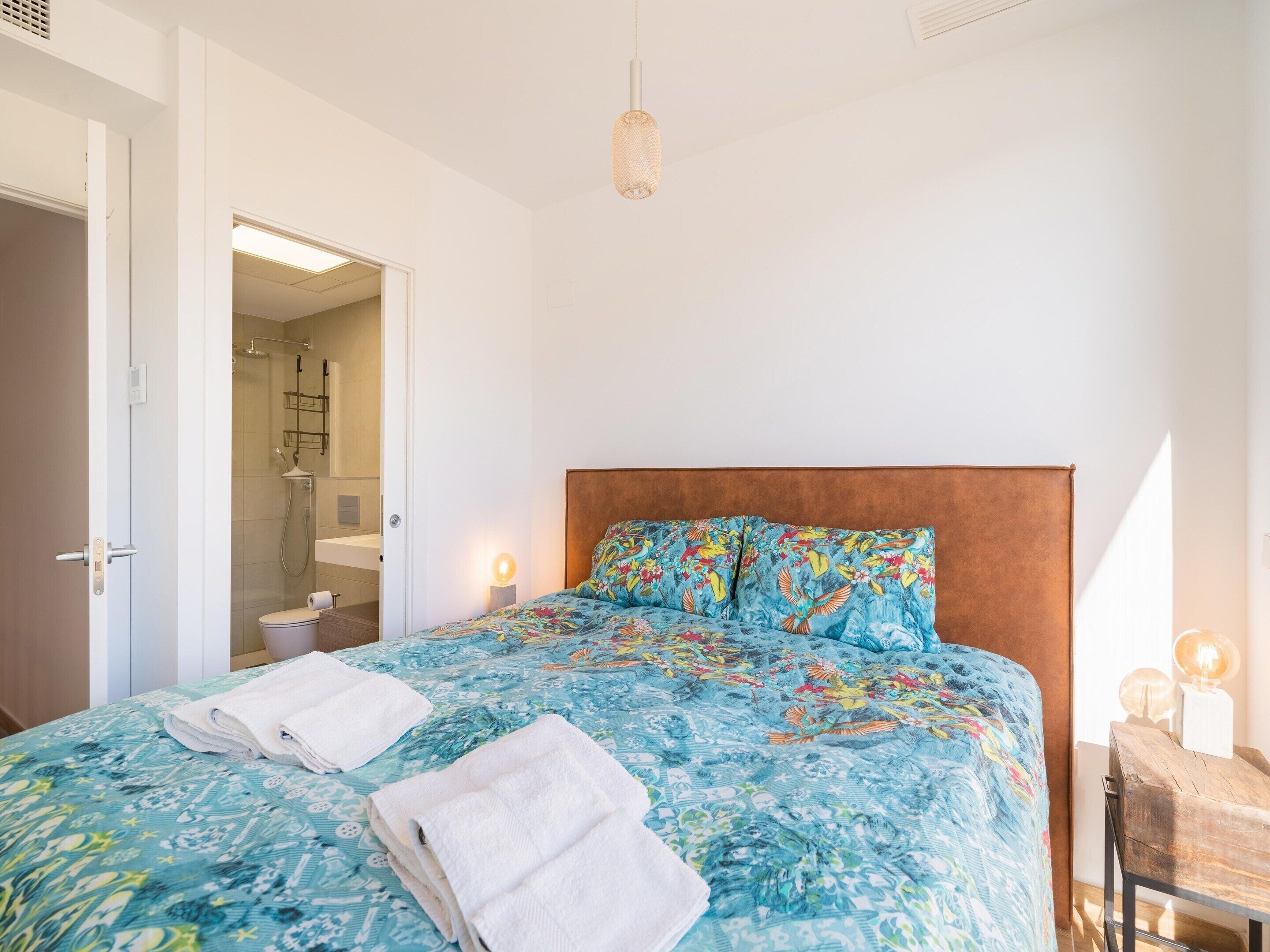 A bedroom with a bed, two towels, a wooden headboard, and a hanging light fixture.