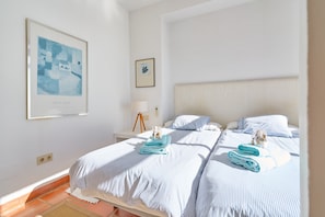 Una cama bien hecha con ropa de cama a rayas azul y blanco, una obra de arte enmarcada en la pared y una lámpara de noche.