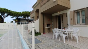 A patio with a table and chairs, a grill, and a pool in the background. - Belvilla by OYO Appartamento Nero (Jesolo)