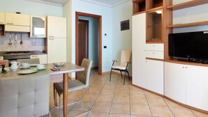 A compact kitchen with a dining area, a TV, and a door leading to another room. - Belvilla by OYO Appartamento Nero (Jesolo)