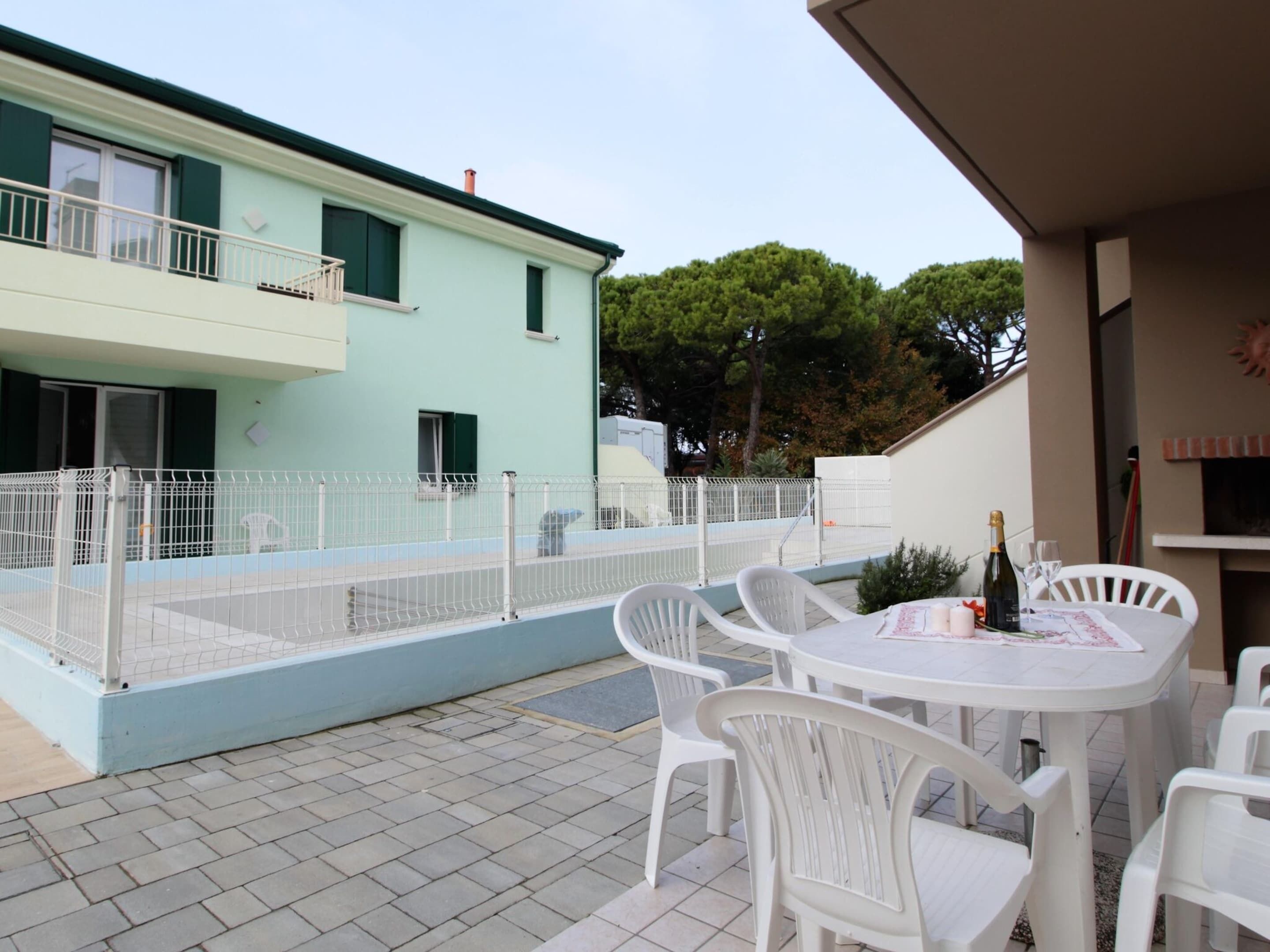 Eine Terrasse mit weißen Plastikstühlen und einem Tisch, ein Gebäude mit hellblauer Fassade und ein weißer Zaun.