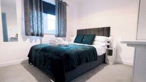 A modern bedroom with a large bed, a nightstand, a bedside table, and a window with curtains.