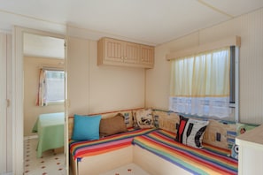 A compact room with a bed, a small table, a cabinet, and a window with curtains.
