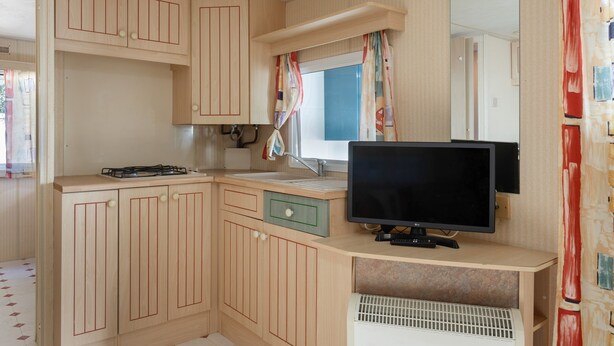 Een compacte keuken met houten kastjes, een gootsteen, een fornuis en een flatscreen televisie.