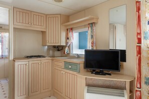 Una cocina compacta con armarios de madera, un lavamanos, una estufa y un televisor de pantalla plana.