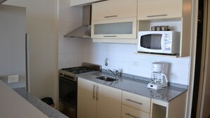 A compact kitchen with a gas stove, oven, microwave, and coffee maker. - Terrazas del lago I U with a view of Nahuel Huapi Lake (San Carlos de Bariloche)