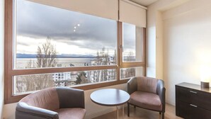A room with a large window, two chairs, a small table, and a cabinet. - Terrazas del lago I U with a view of Nahuel Huapi Lake (San Carlos de Bariloche)