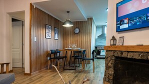 Een moderne woonkamer met een houten wandpaneel, een eethoek met een tafel en stoelen, een open haard en een televisie waarop streaming apps worden weergegeven.