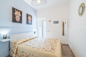 A bedroom with a bed, a nightstand, a wall-mounted mirror, and artwork.