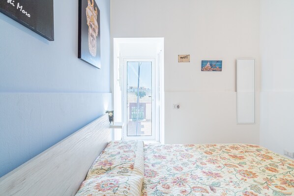 Une chambre avec un lit, une porte donnant sur un espace extérieur, une œuvre d’art accrochée au mur et un petit panneau indiquant la disponibilité du Wi-Fi.