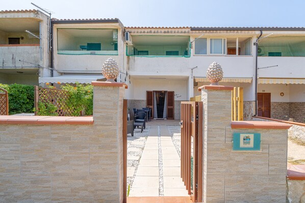 A multi-story building with balconies, a gated entrance, and a stone wall.