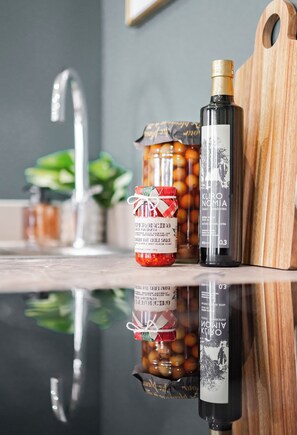 A kitchen counter with a bottle of Kuro Nomia, a jar of peperoncino, and a wooden cutting board.