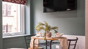 Un comedor con una mesa dispuesta para dos personas, una planta en maceta y un televisor montado en la pared.