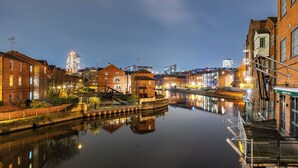 Un río tranquilo que refleja edificios, un puente y un rascacielos moderno al fondo.
