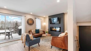 Una sala moderna con chimenea, un televisor montado en la pared y un amplio ventanal con vistas a una terraza nevada.