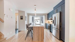 Una cocina moderna con una isla central, muebles oscuros, electrodomésticos de acero inoxidable y vistas al exterior.