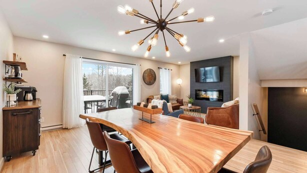 Un moderno salón con una mesa de comedor de madera, asientos cómodos, una chimenea y un televisor montado en la pared.
