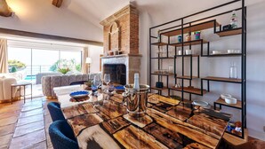 Un coin repas avec une table en bois rustique, une cheminée en briques et une étagère moderne où sont exposés des verres.
