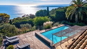 Un espace piscine offrant une vue sur la mer, entouré d’une végétation luxuriante et de palmiers.