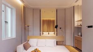 Et moderne hotelværelse med en stor seng, en hvid sofa, et lille bord med en skål frugt og en sengebordlampe.