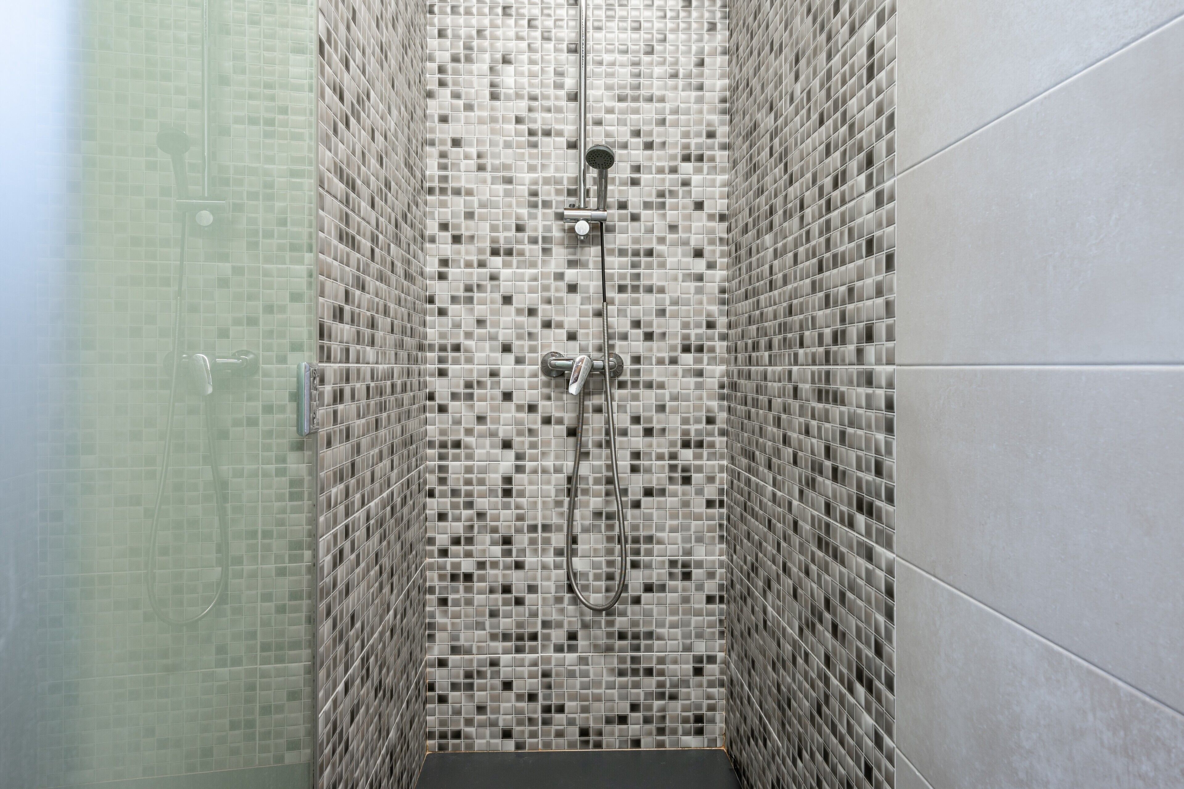 A shower with a tiled wall and a metal showerhead.