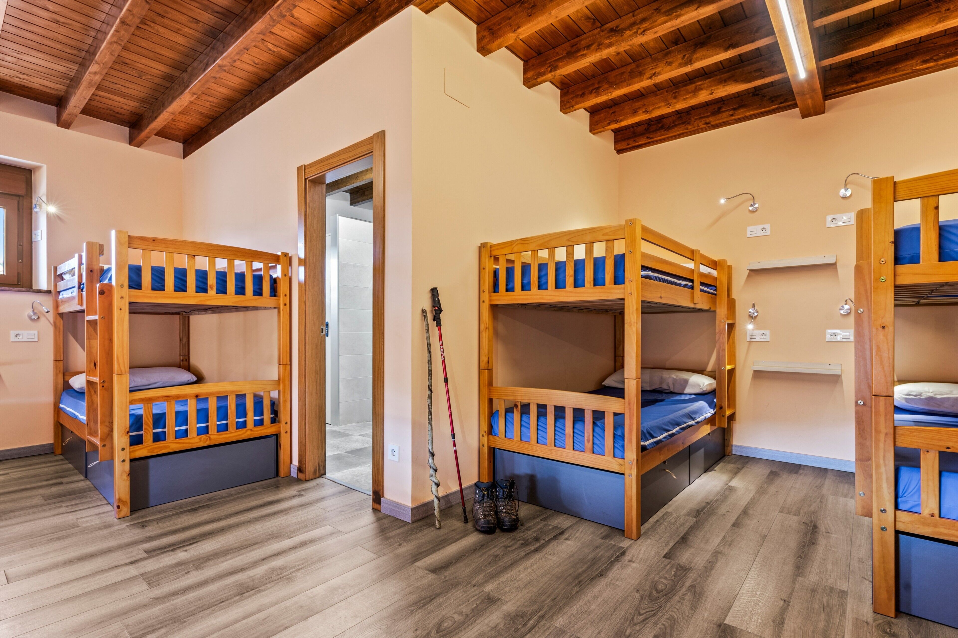 A room with bunk beds, wooden flooring, a door, and a window.