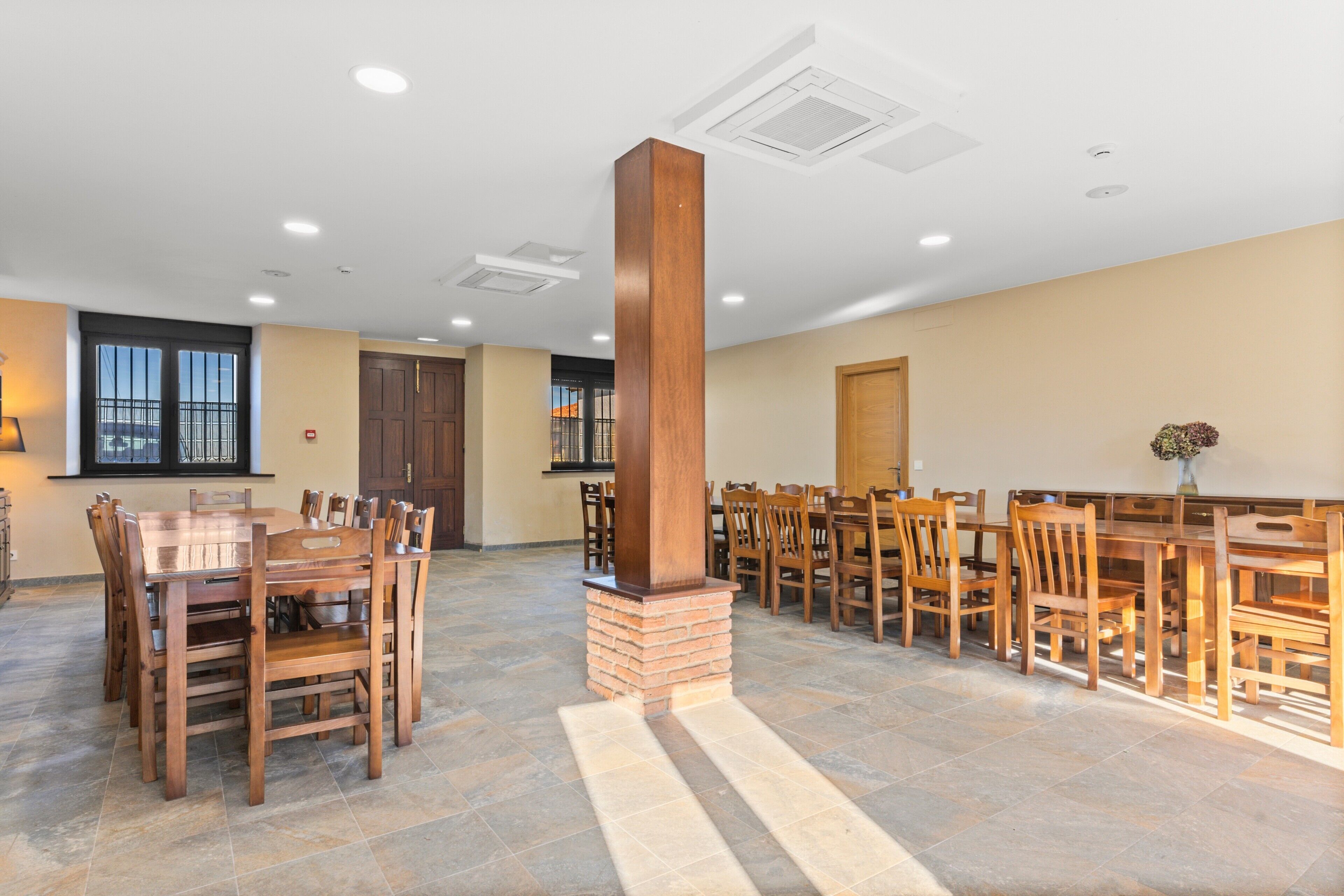 A spacious dining area with wooden tables and chairs, a central pillar, and a tiled floor.