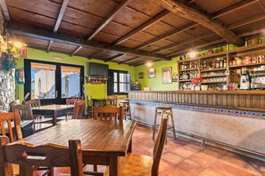 Ein Restaurant mit Holztischen und -stühlen, einer Bar mit Flaschenregalen und einer grünen Wand mit einem Fenster.
