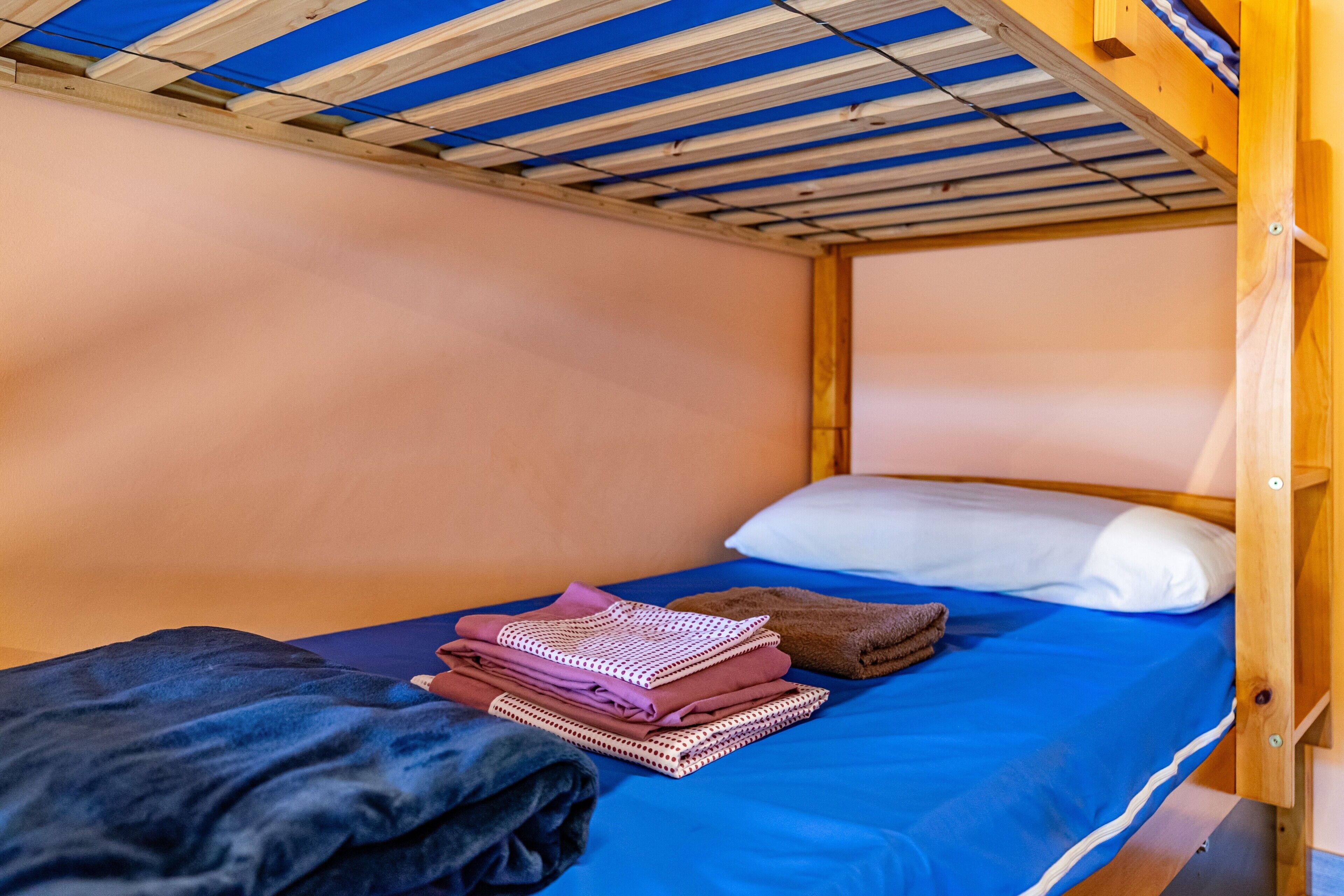 Een stapelbed met een blauwe matras, een wit kussen en opgevouwen kleding op het bed.
