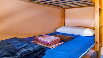 Een stapelbed met een blauwe matras, een wit kussen en opgevouwen kleding op het bed.