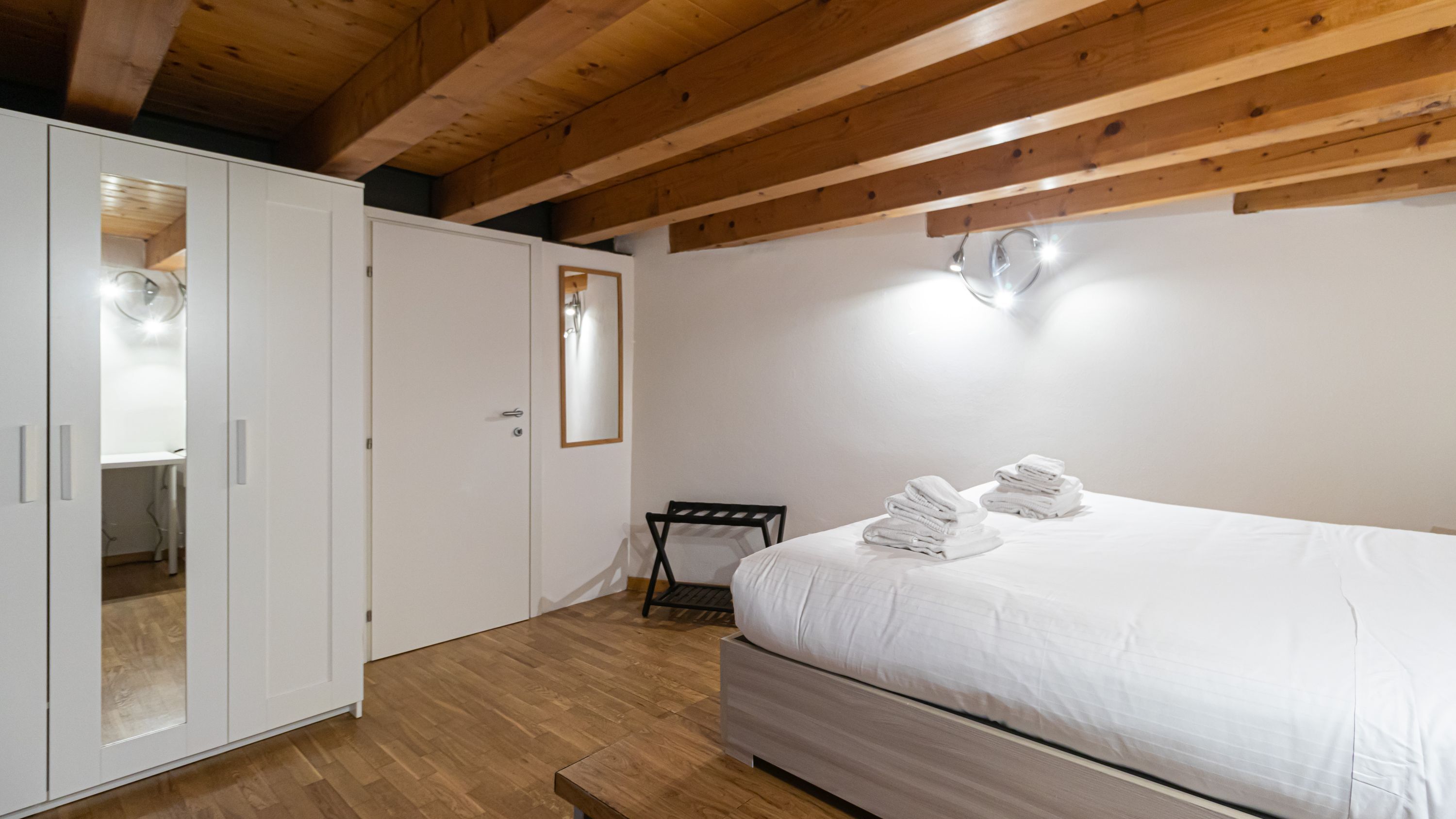 Een slaapkamer met een bed, een witte kast en een klein tafeltje met handdoeken.