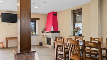 Un comedor con chimenea de ladrillo, sillas de madera y televisor montado en la pared.