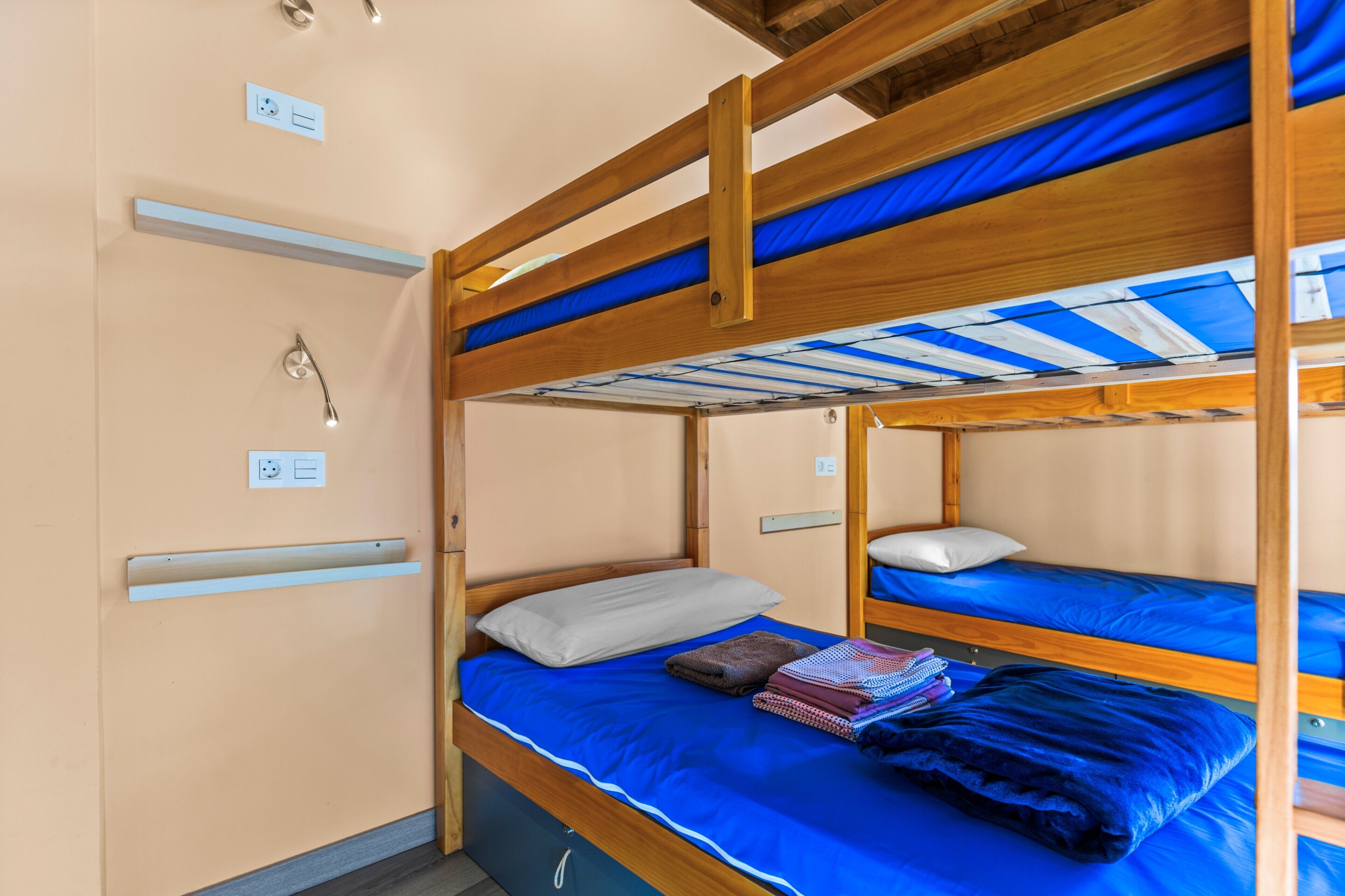 Habitación con literas de madera, colchón azul y almohada blanca.
