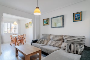 Uma sala de estar com sofá, mesa de madeira e área de jantar com cadeiras.
