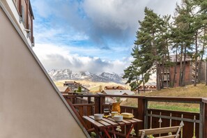 A wooden deck with a table set for dining, overlooking a mountainous landscape with buildings in the background.