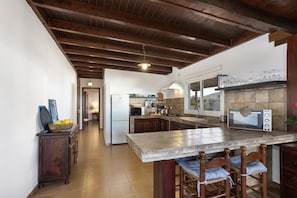 A kitchen with a tiled island, wooden chairs, a microwave, and a refrigerator.