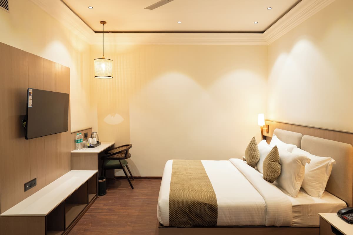 A hotel room with a bed, bedside table, TV, desk, chair, and a lamp.