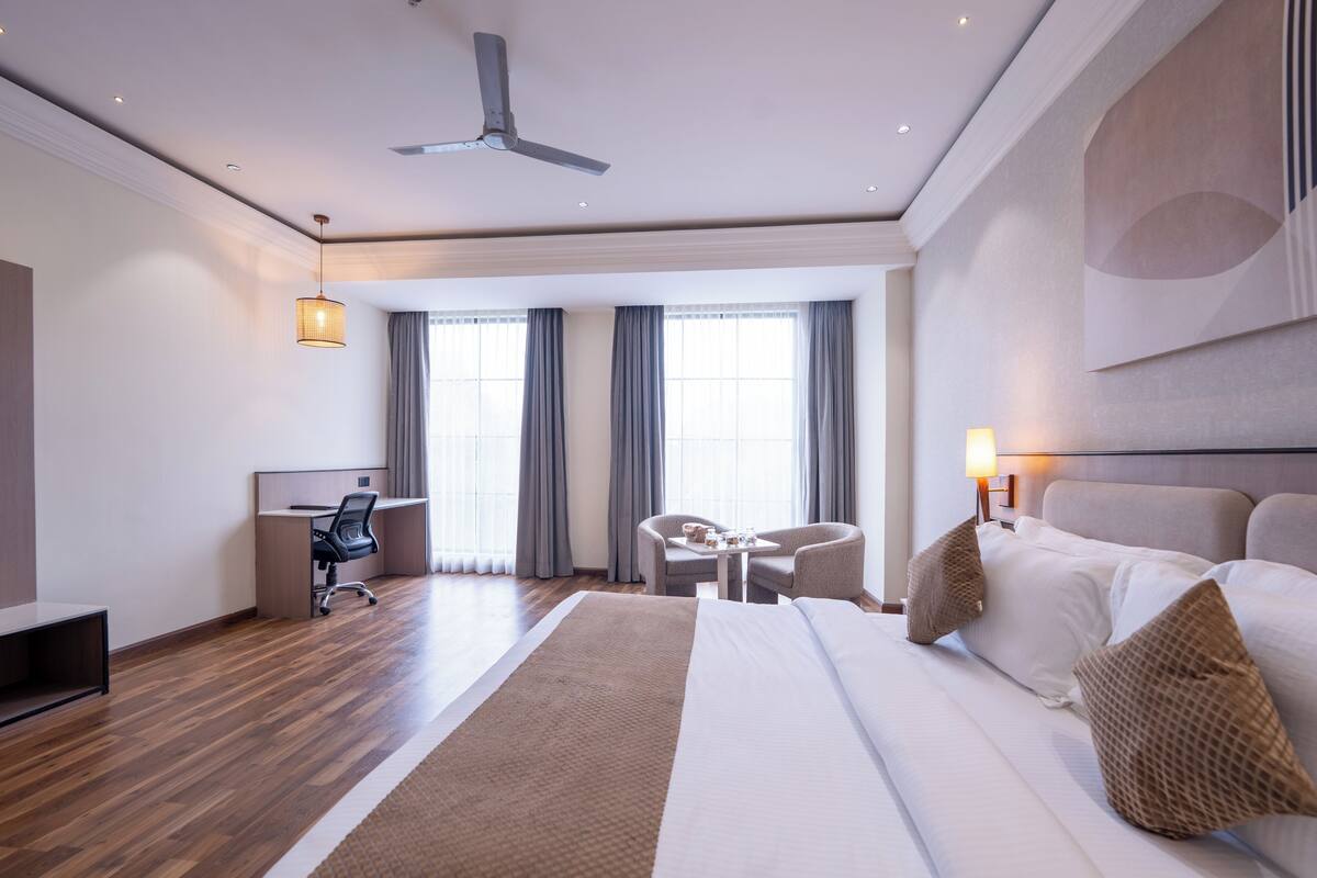 A modern hotel room with a large bed, a desk, a chair, and a small table.