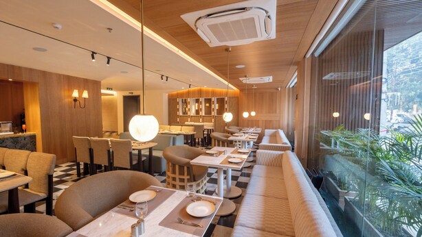 A modern restaurant with a checkered floor, long communal tables, and a seating area with cushioned benches. - Ramee ColleXtion Amritsar, Near Golden Temple (Amritsar)