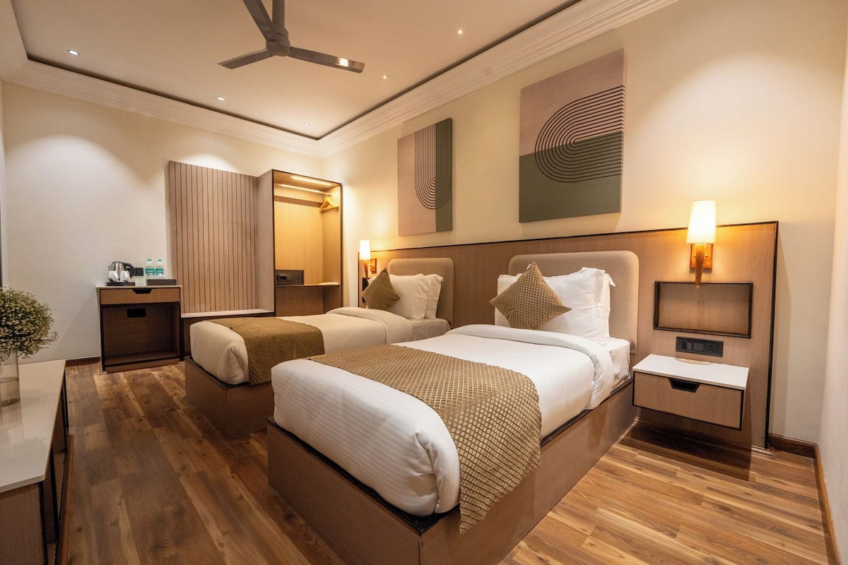 A modern hotel room with two beds, a desk, a mirror, and artwork on the walls.