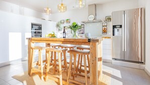 A modern kitchen with a wooden island, bar stools, pendant lights, a stainless steel refrigerator, and a built-in oven. - Vacation Home "Mimar Urban Altea Sol" with Sea View, Private Terrace & Wi-Fi (Altea)