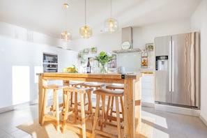Una cucina moderna con isola in legno, sgabelli da bar, luci a sospensione, frigorifero in acciaio inossidabile e forno integrato.