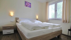 A bedroom with a wooden bed, two bedside tables, a night light, and a window with curtains. - Appartement Hafenflair am Plauer See (Plau am See)