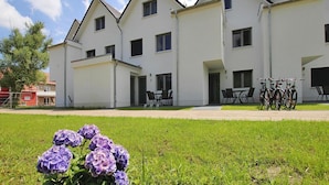 A modern building with multiple windows and doors, a grassy lawn in the foreground, and bicycles parked outside. - Appartement Hafenflair am Plauer See (Plau am See)