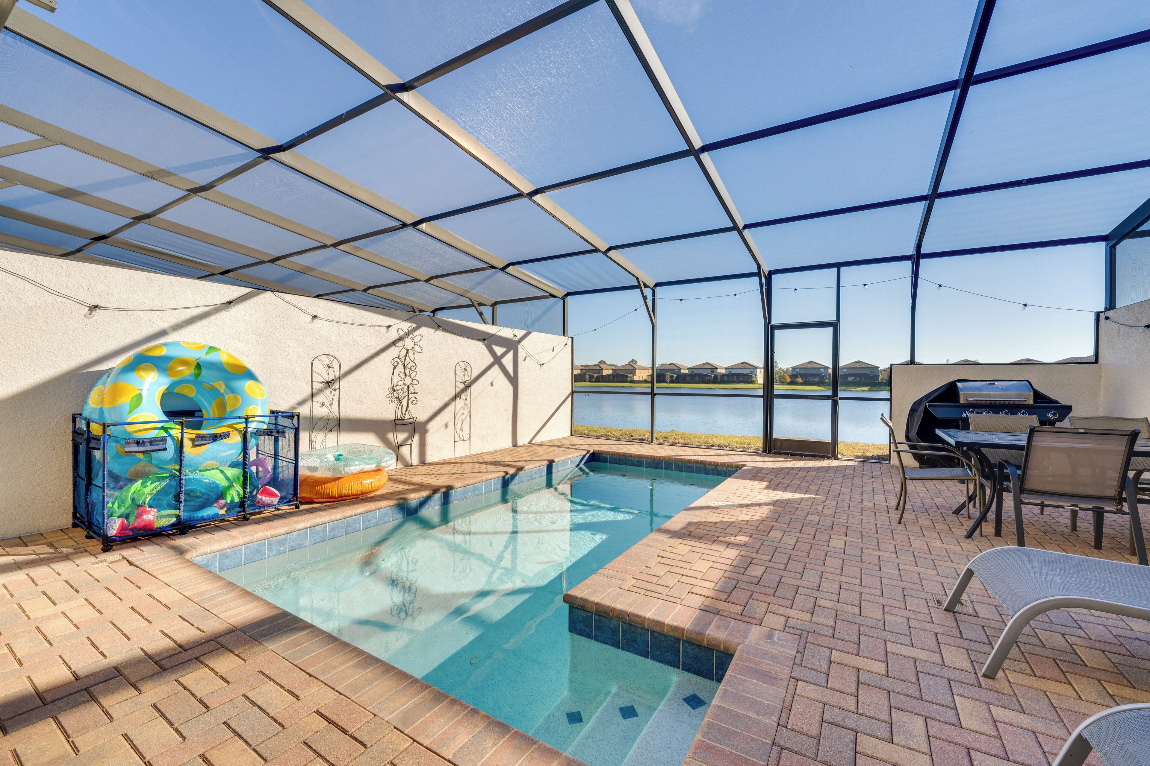 An indoor pool area with a view of a lake, a barbecue grill, and a covered seating area.