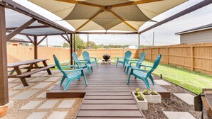 Eine überdachte Terrasse mit Holzboden, türkis-farbenen Stühlen und einem Feuerkorb in der Mitte.