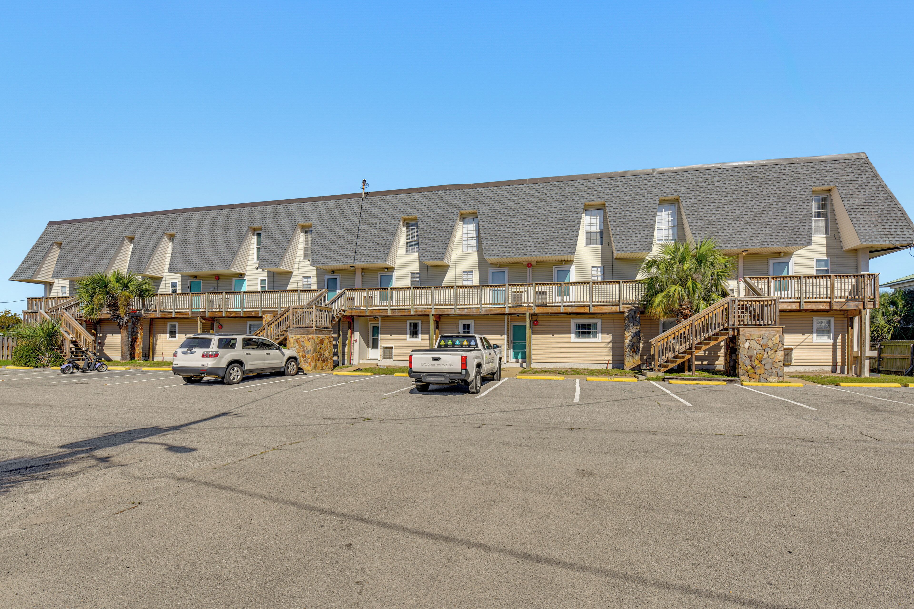 A motel with a long, flat roof and multiple windows. There are two cars parked in the parking lot.