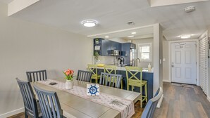 A dining area with a table set for six, surrounded by chairs, and a kitchen in the background. - Walk to Okaloosa Island Beach: Coastal Condo! (Fort Walton Beach)