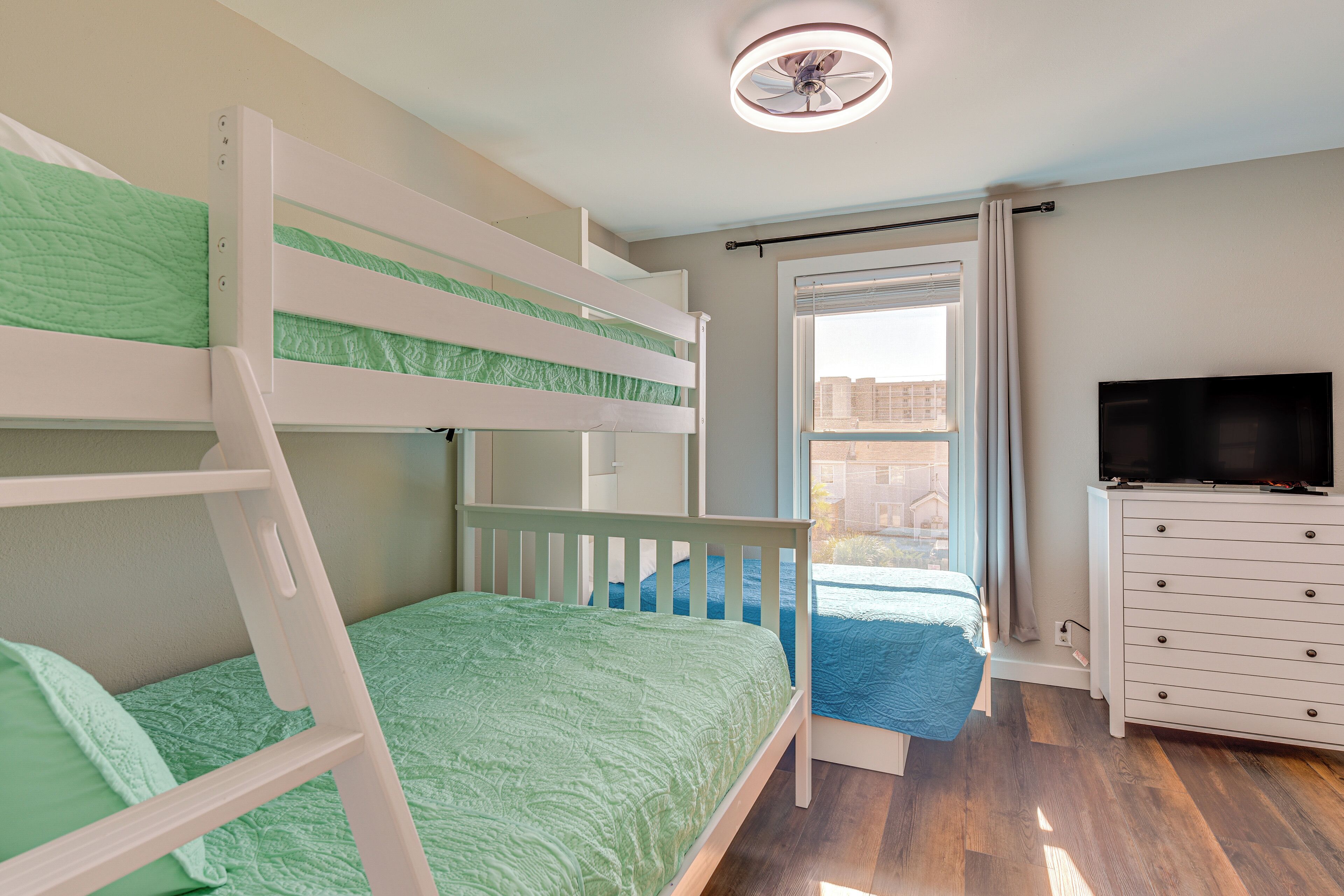 A bunk bed room with a TV and dresser.